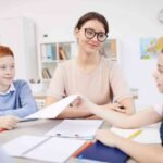 9bbe17c662535ed1c99a36c6f40fb780-teacher-sits-with-a-group-of-kids-in-a-classroom_l