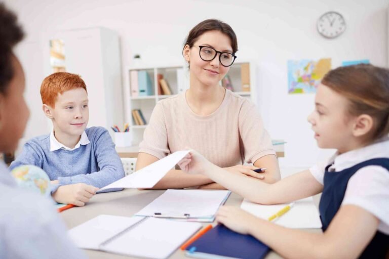 9bbe17c662535ed1c99a36c6f40fb780-teacher-sits-with-a-group-of-kids-in-a-classroom_l
